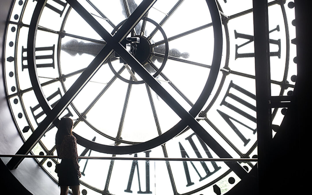 a-woman-stands-at-the-back-of-a-massive-white-clock-face_s-1080x675